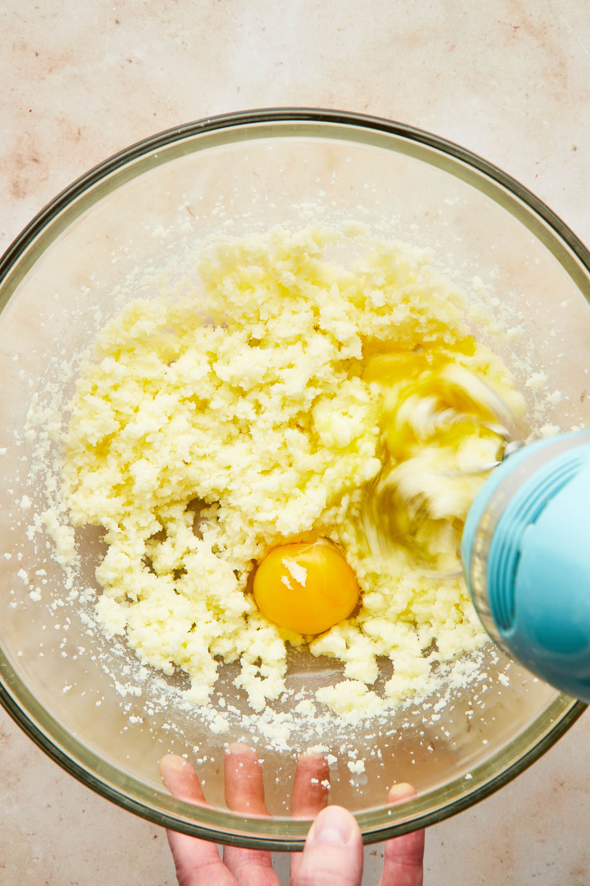 A hand using a hand mixer to beat eggs into creamed butter.