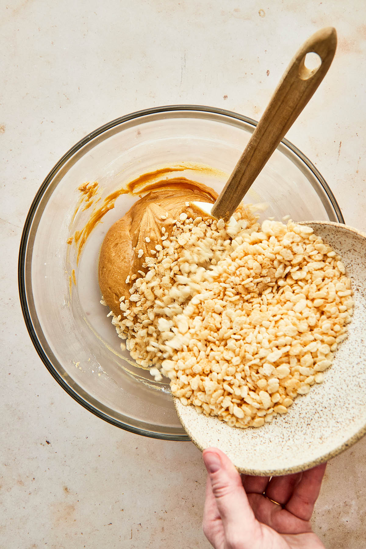 A bowl of crispy rice cereal being poured into a bowl of peanut butter.