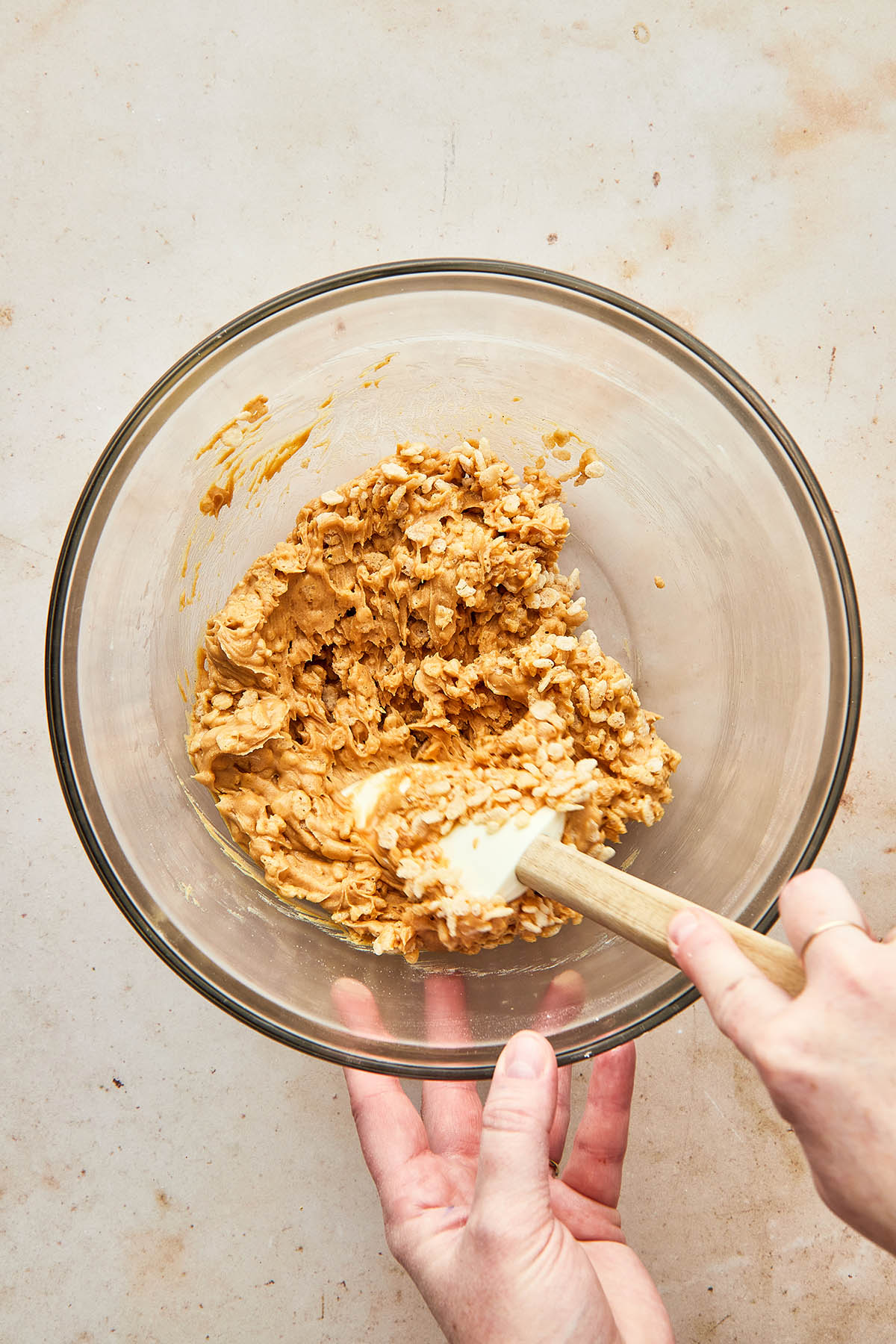 A hand using a rubber spatula to stir cereal and peanut butter together.