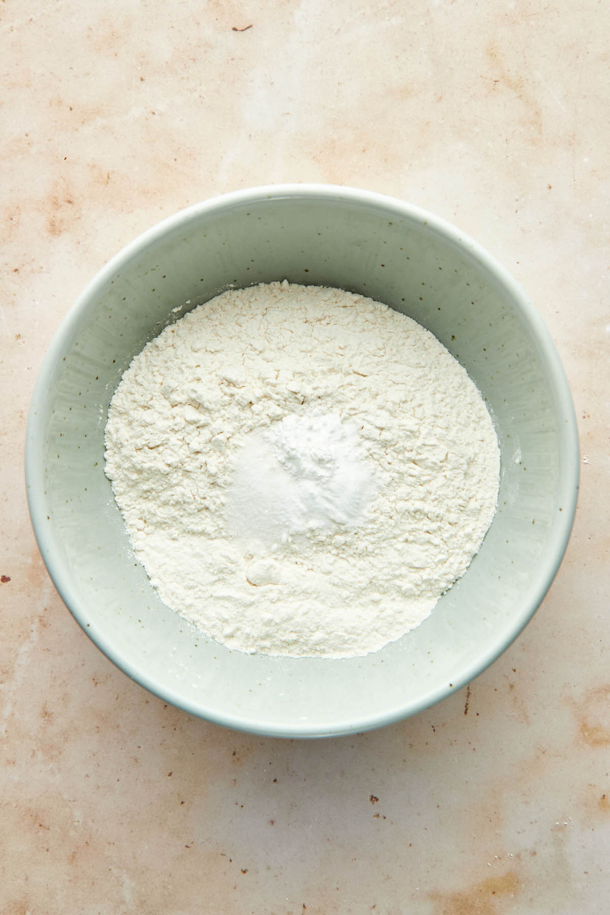 Unmixed flour, baking powder, baking soda, and salt in a light blue mixing bowl.