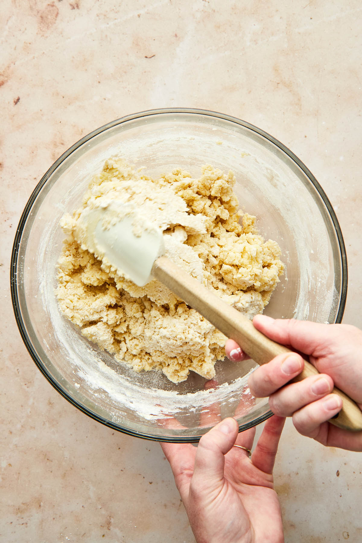 A hand using a rubber spatula to mix any remaingin dry flour bits into a bowl of cookie dough.