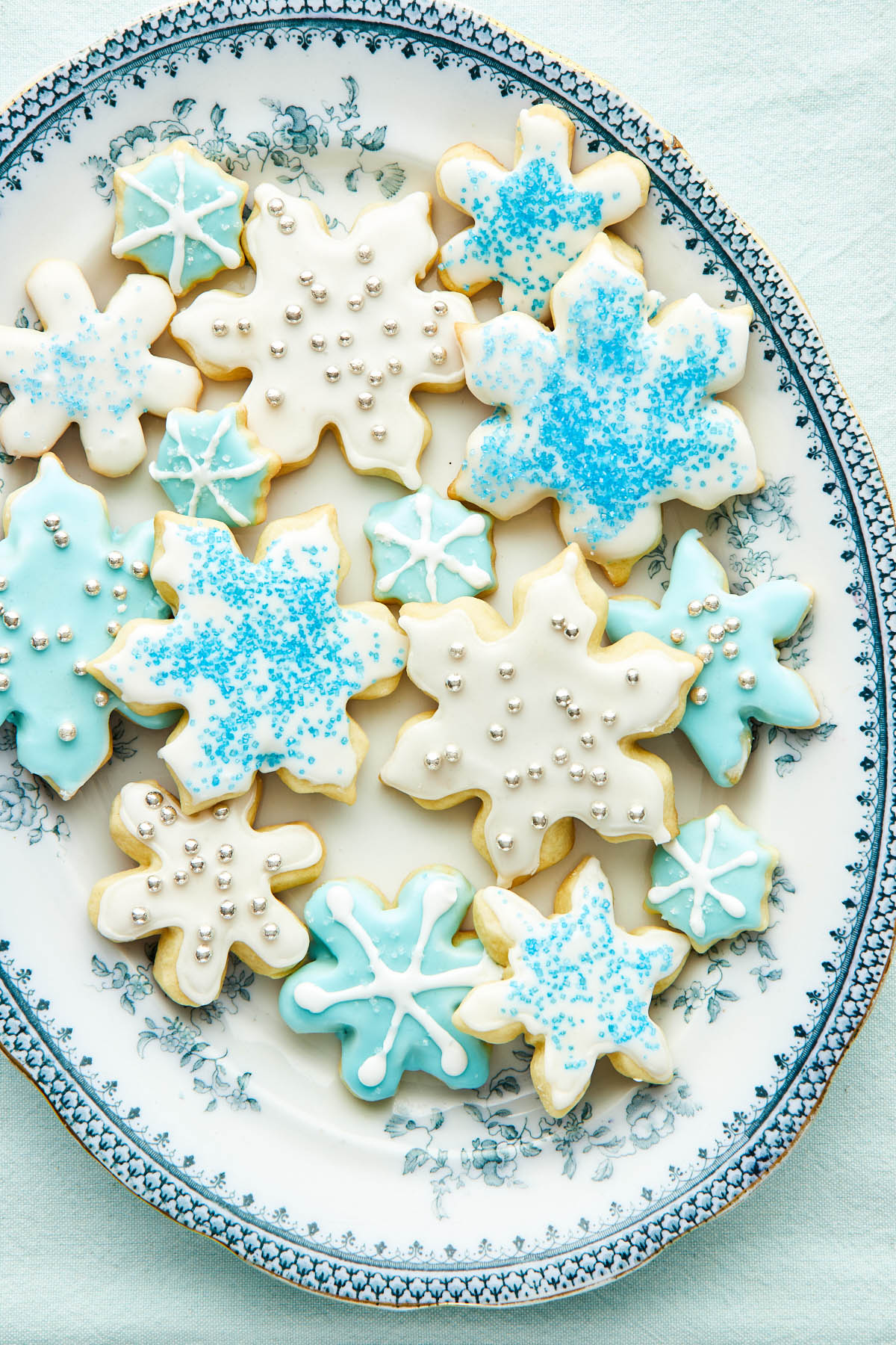 A large oval dish with blue trim topped with decorated snowflake sugar cookies.