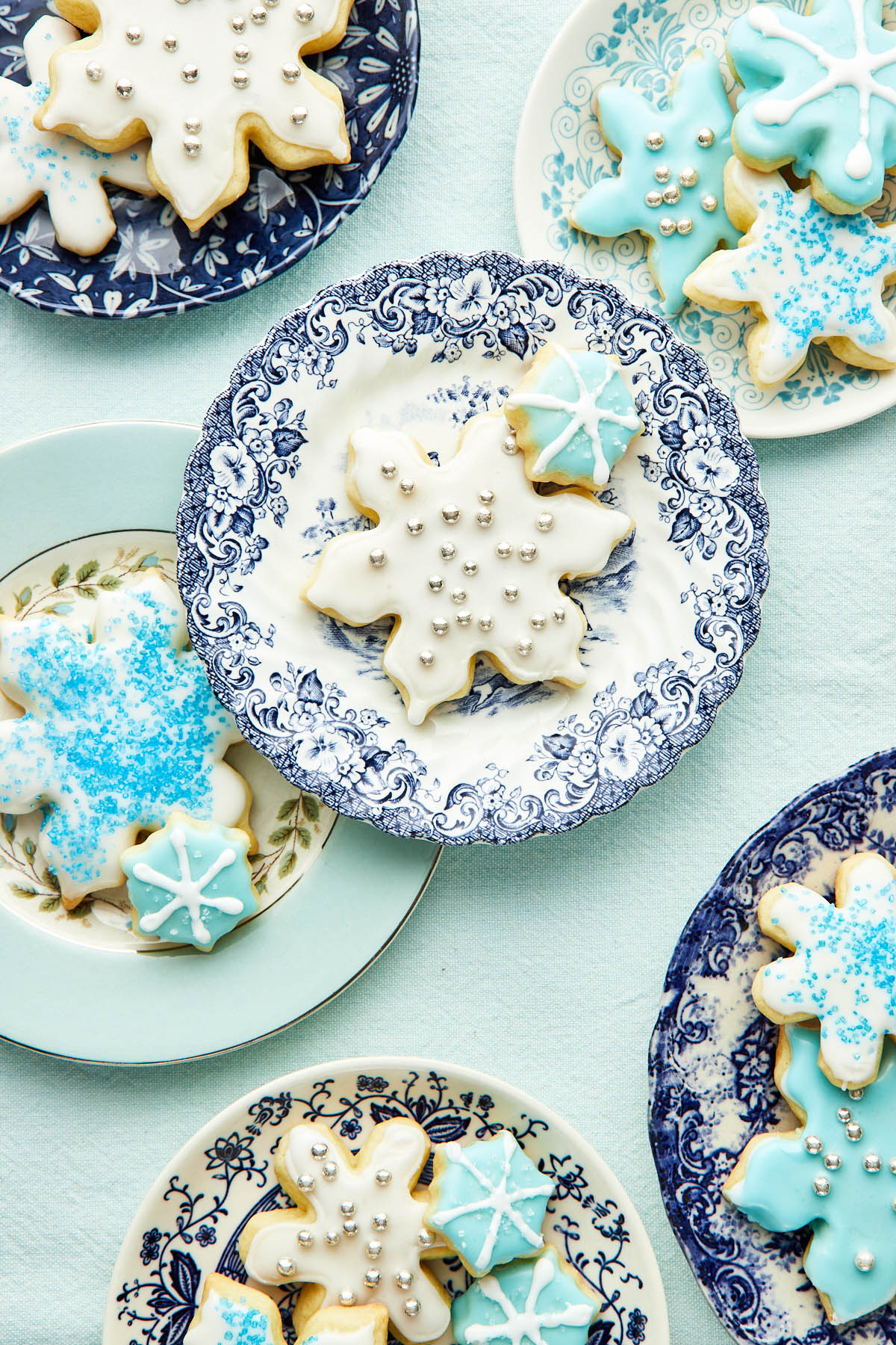 A variety of blue and white plates topped with different-sized snowflake sugar cookies.