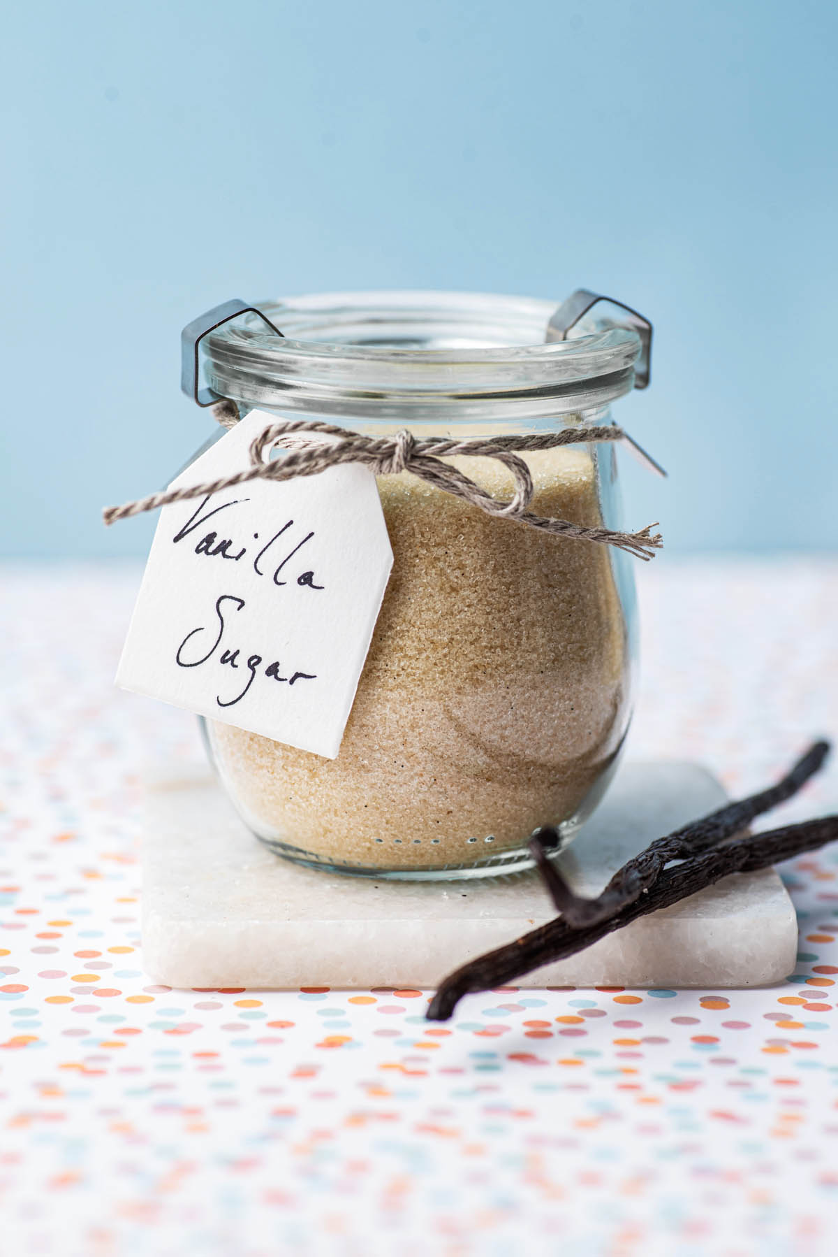 A small jar of vanilla sugar on a small marble board with whole vanilla beans laying alongside the jar.