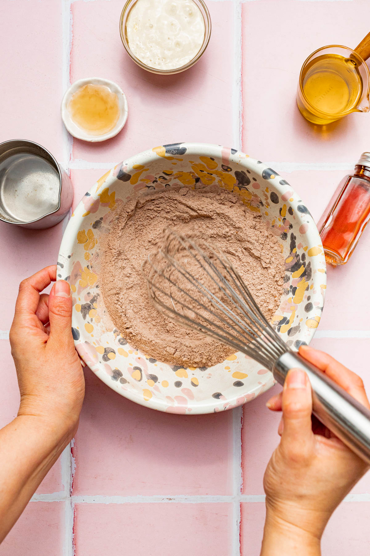 A hand using a whisk to mix dry ingredients in a mixing bowl.