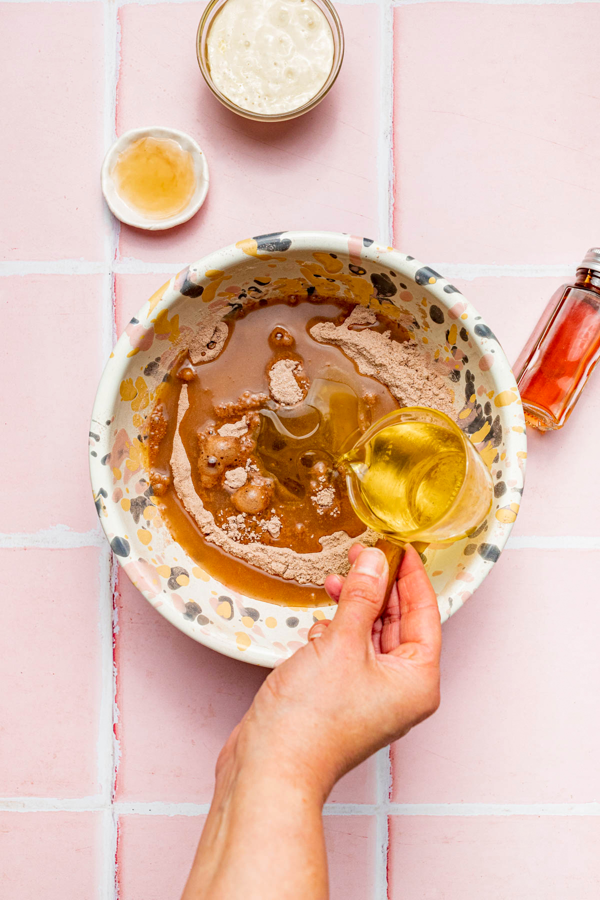 A hand pouring oil from a measuring cup into a bowl of cake ingredients.
