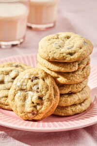 A stack of sourdough chocolate chip cookies on a pink plate with two glasses of milk in behind.