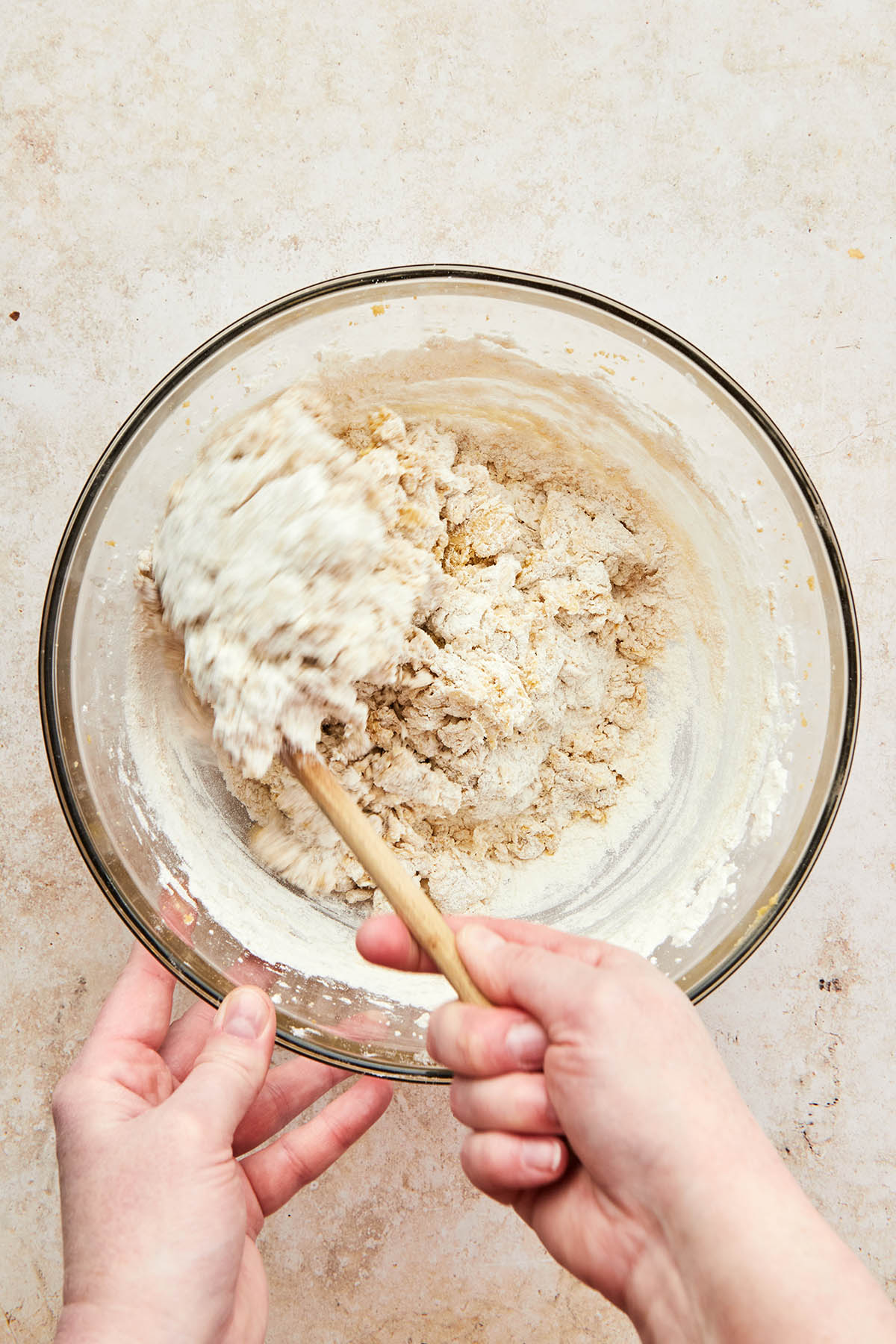 A hand mixing cookie dough with a wooden spoon.