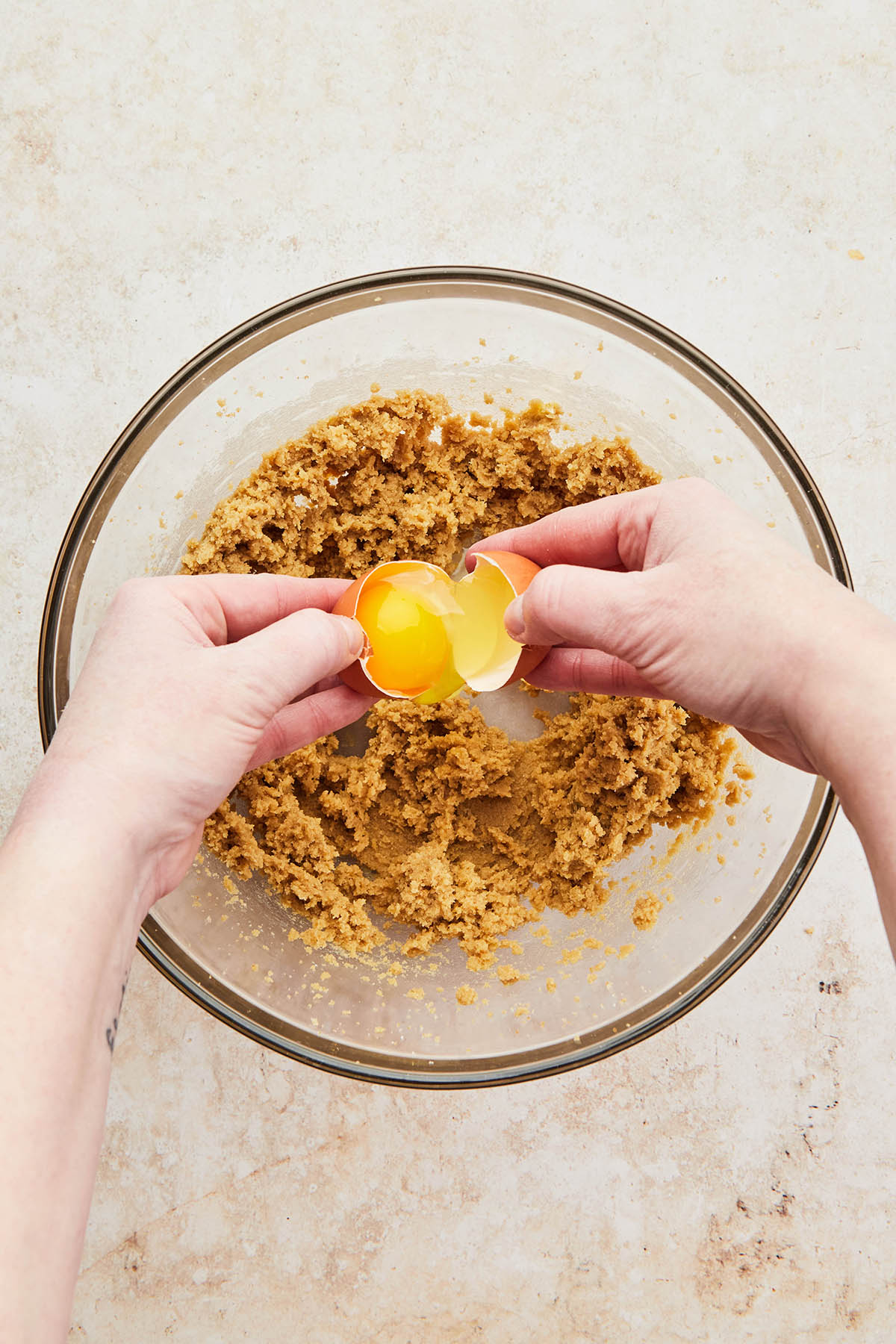 Hands cracking an egg into a bowl of mixed wet ingredients.