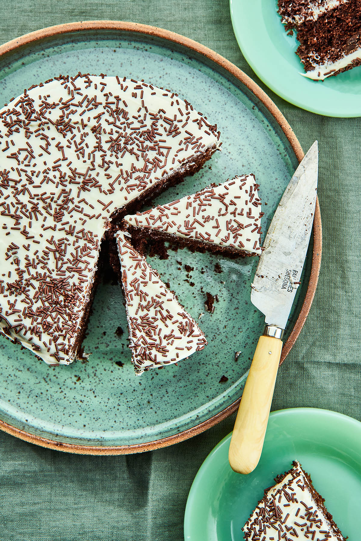 Overhead image of a sliced whole wheat chocolate cake on a green speckled pottery platter with slices of cake on small plates nearby.