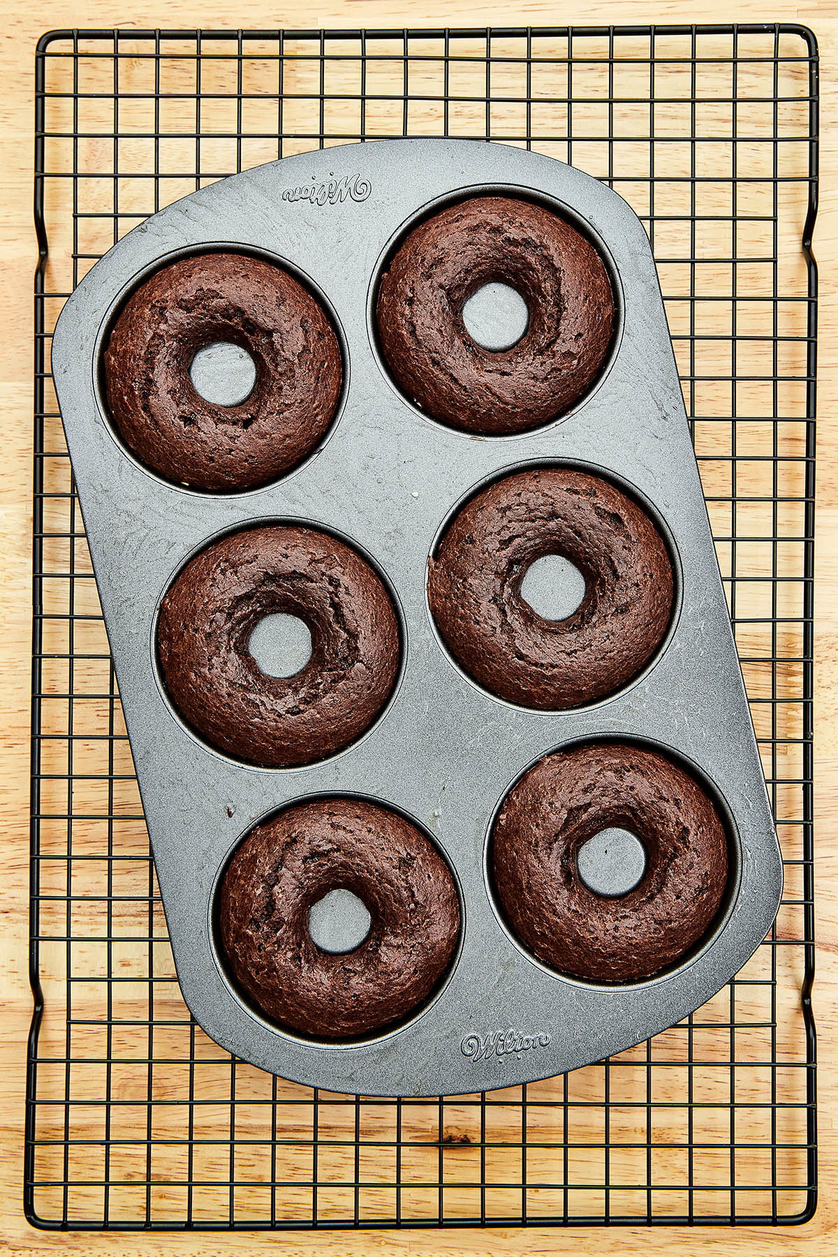 Baked donuts in a tin on a wire cooling rack.