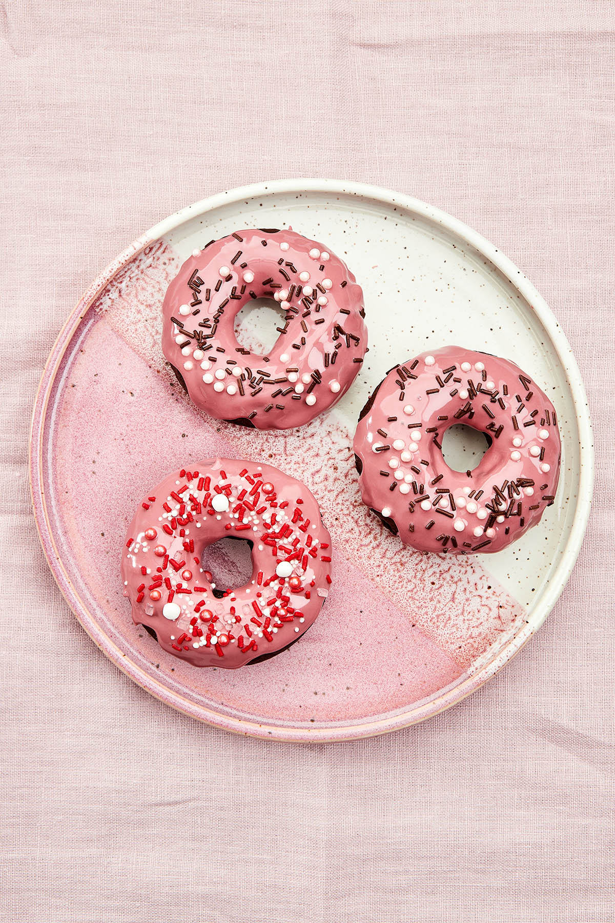 Three chocolate sprinkle donuts on a pink plate.
