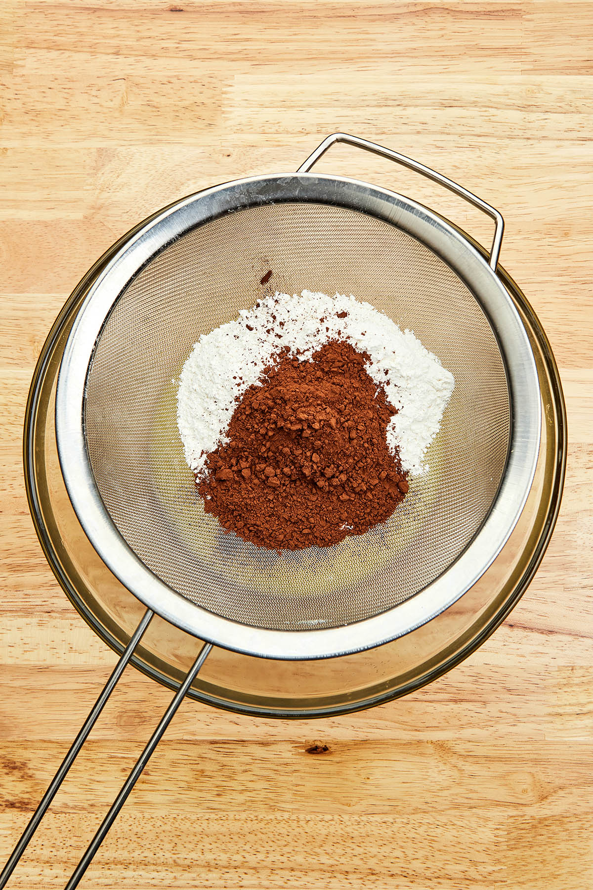 Flour and cocoa in a fine mesh sieve sitting over a mixing bowl.