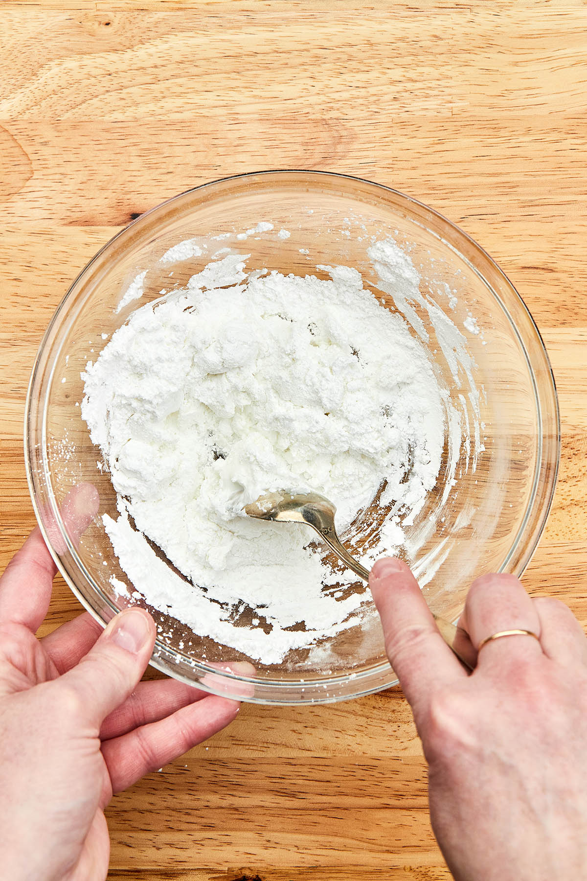 A hand mixing icing with a spoon.