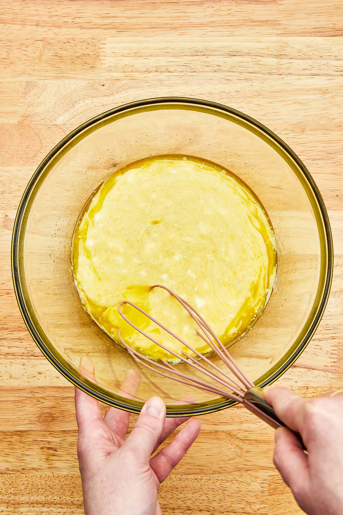 A hand whisking wet cake ingredients in a mixing bowl.