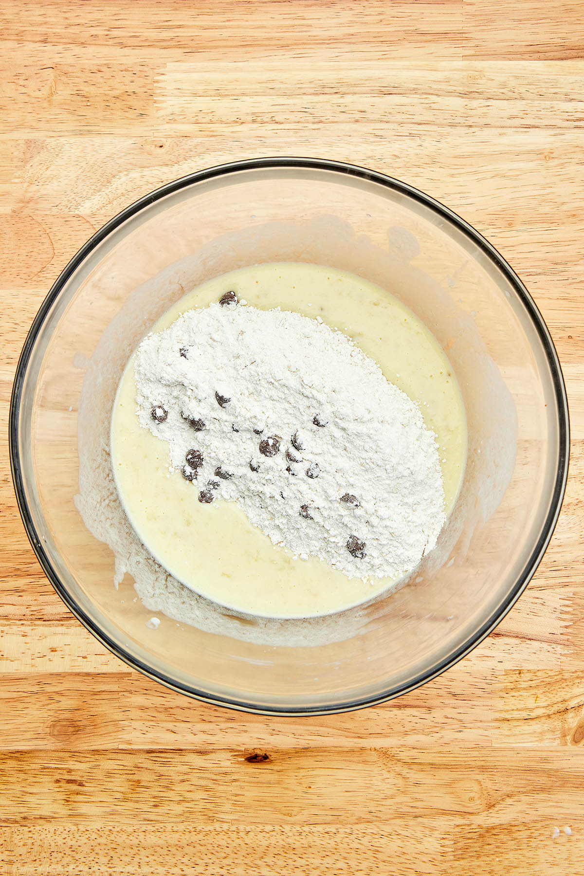 Wet and dry ingredients, unmixed, in a large glass bowl.