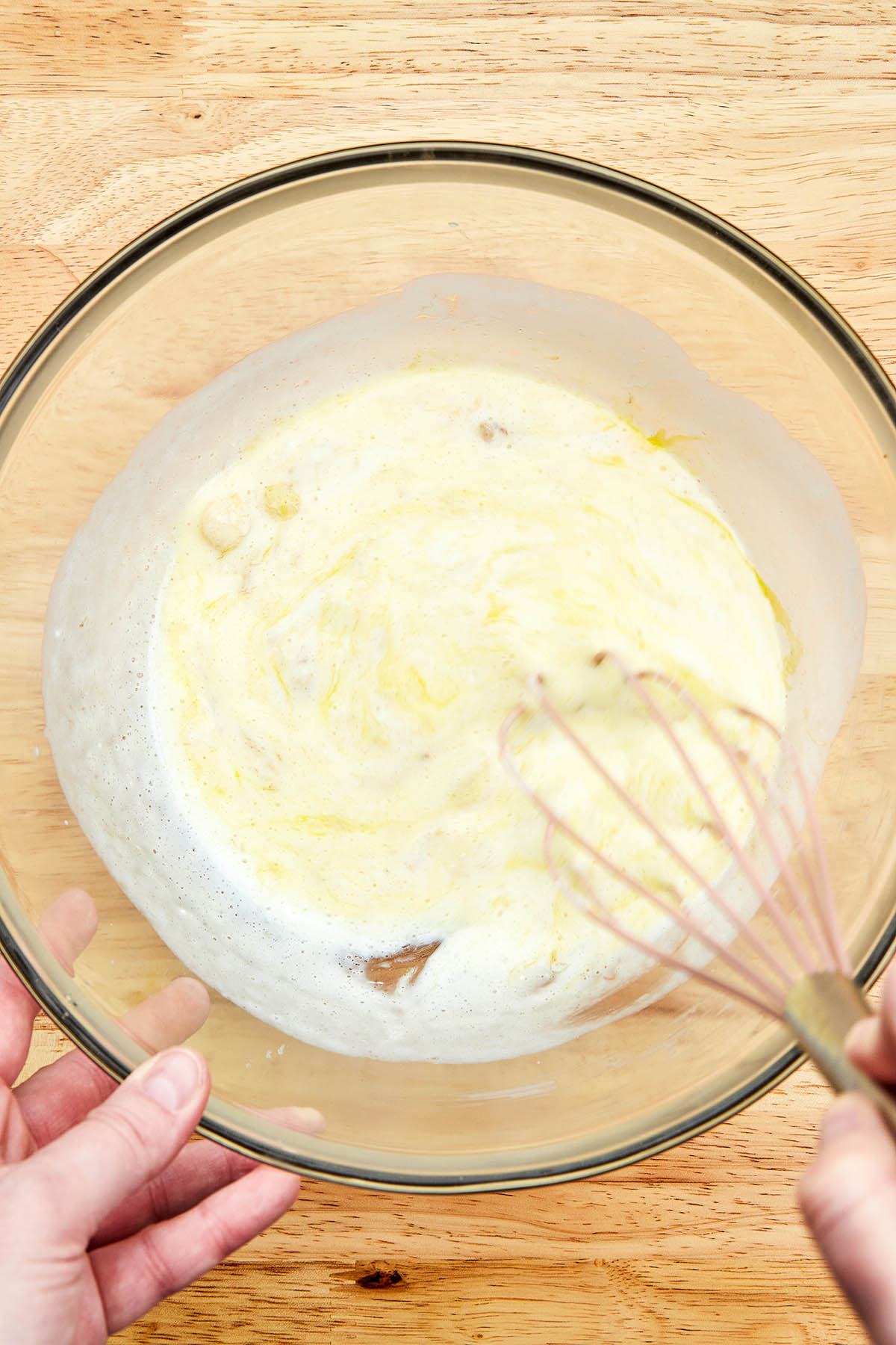 A hand using a whisk to mix wet ingredients.