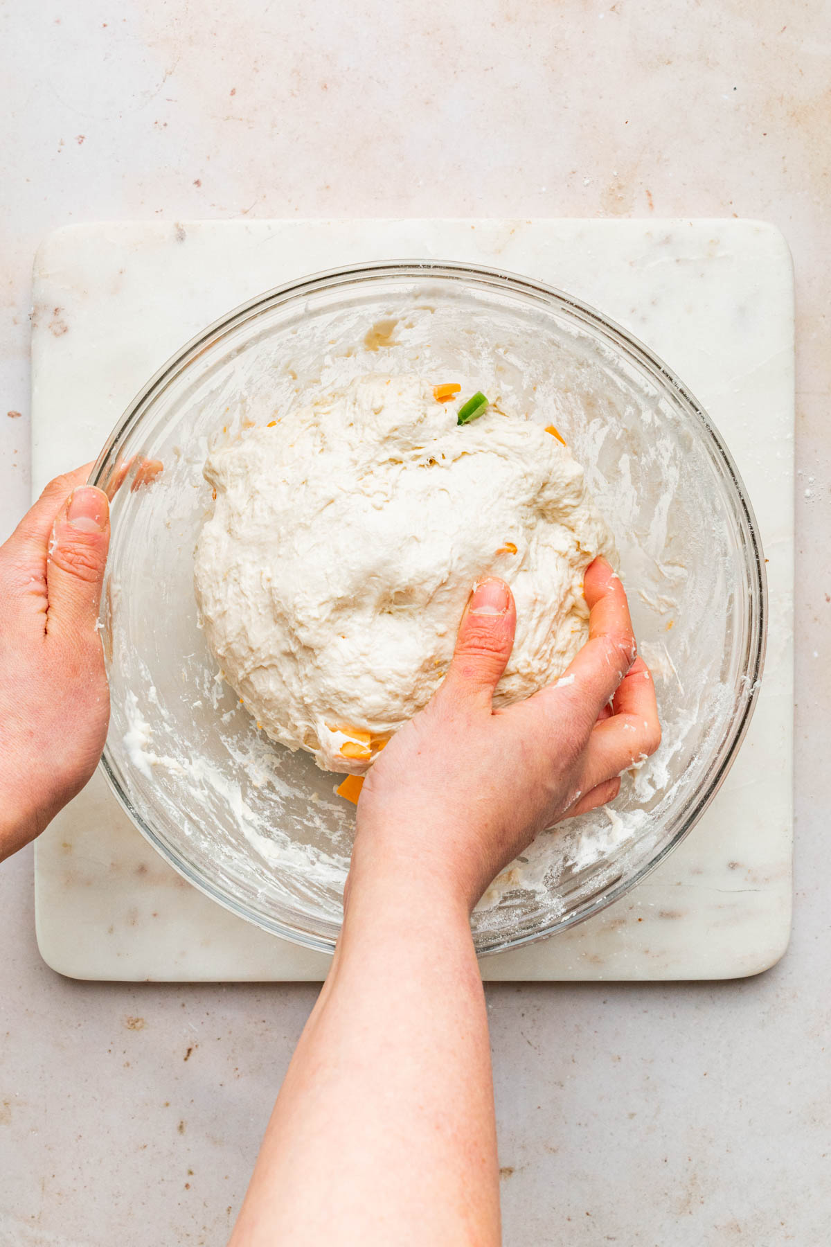 A hand mixing dough in a bowl.