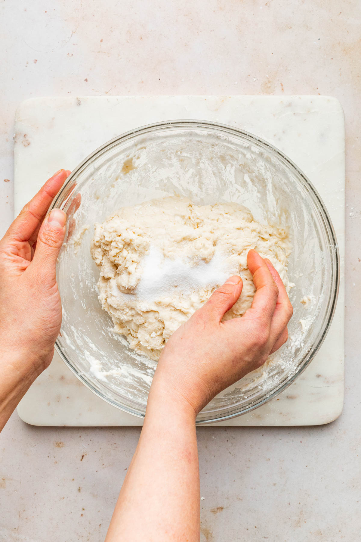 A hand mixing salt into a bowl of dough.