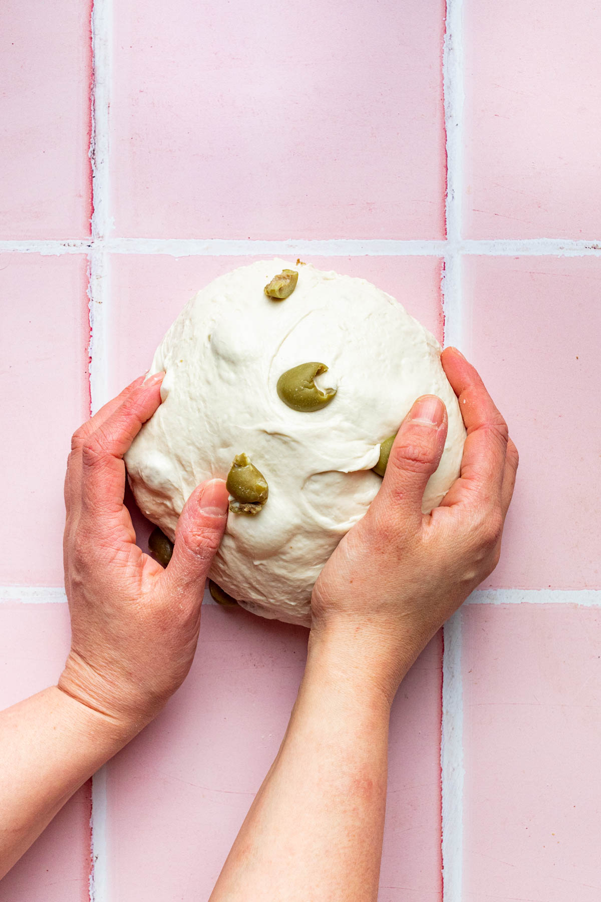 Hands shaping bread dough into a boule shape.