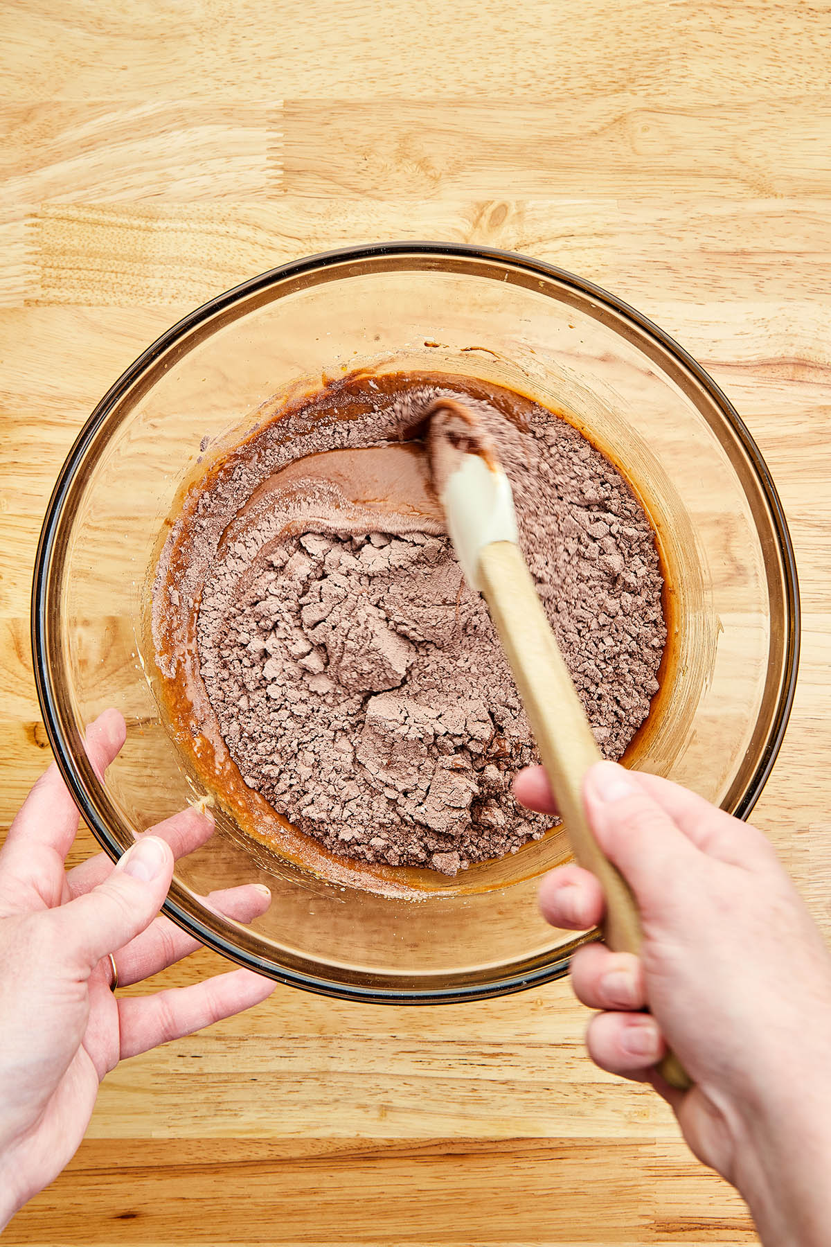 A hand using a rubber spatula to mix flour into chocolate.