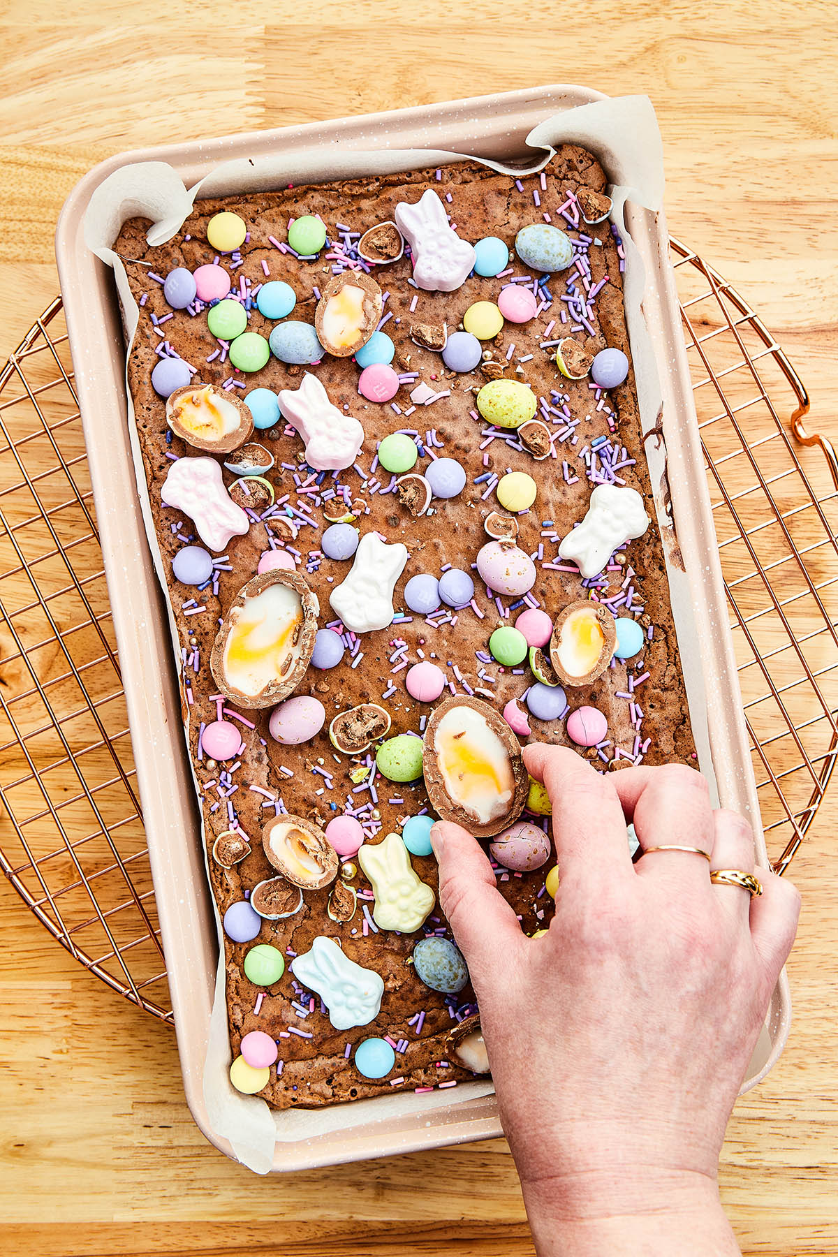 A hand placing a halved fondant egg on top of a pan of brownies.