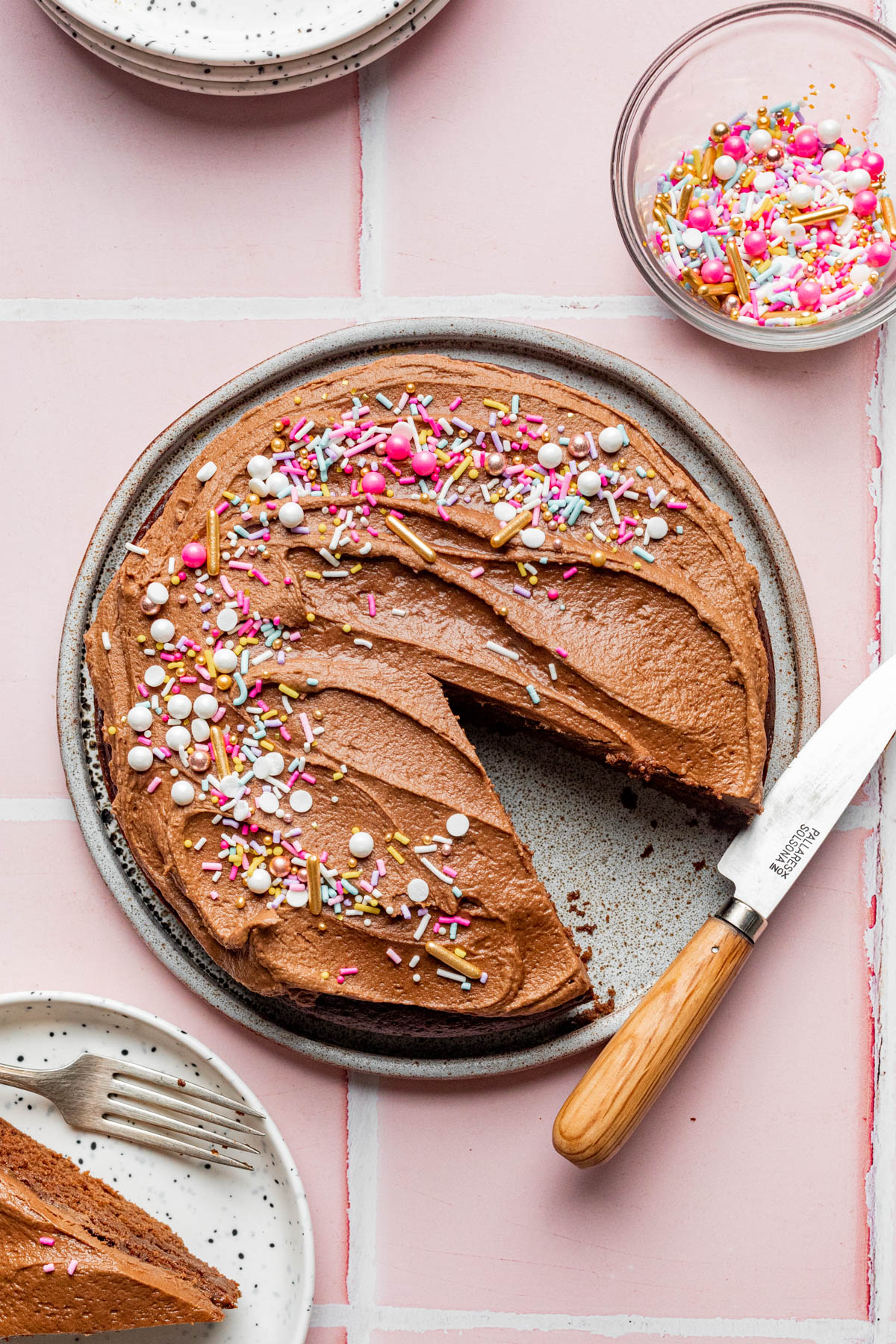 A decorated vegan chocolate cake with one slice cut out with the slice on a small plate nearby with a fork on the plate. a 