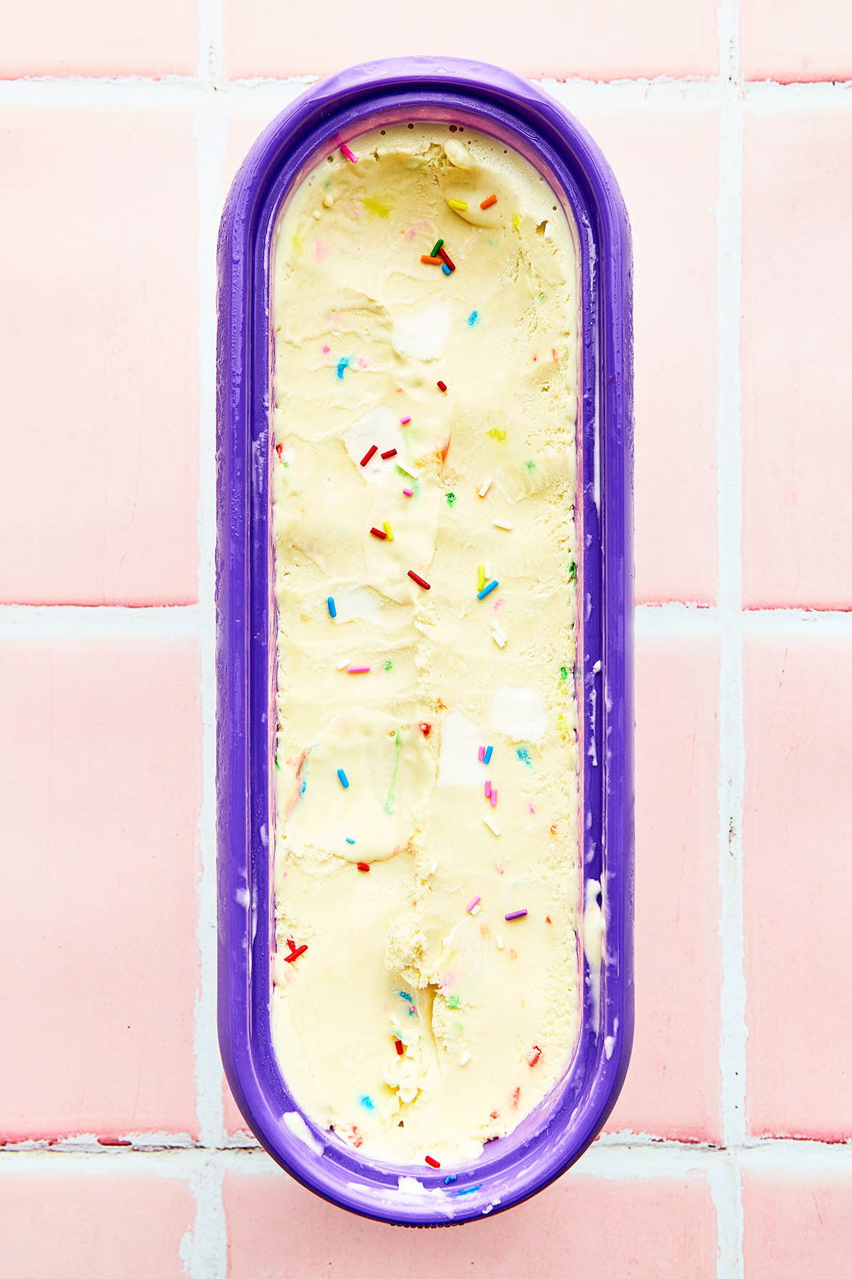 An oblong purple insulated ice cream tub filled with birthday cake ice cream.