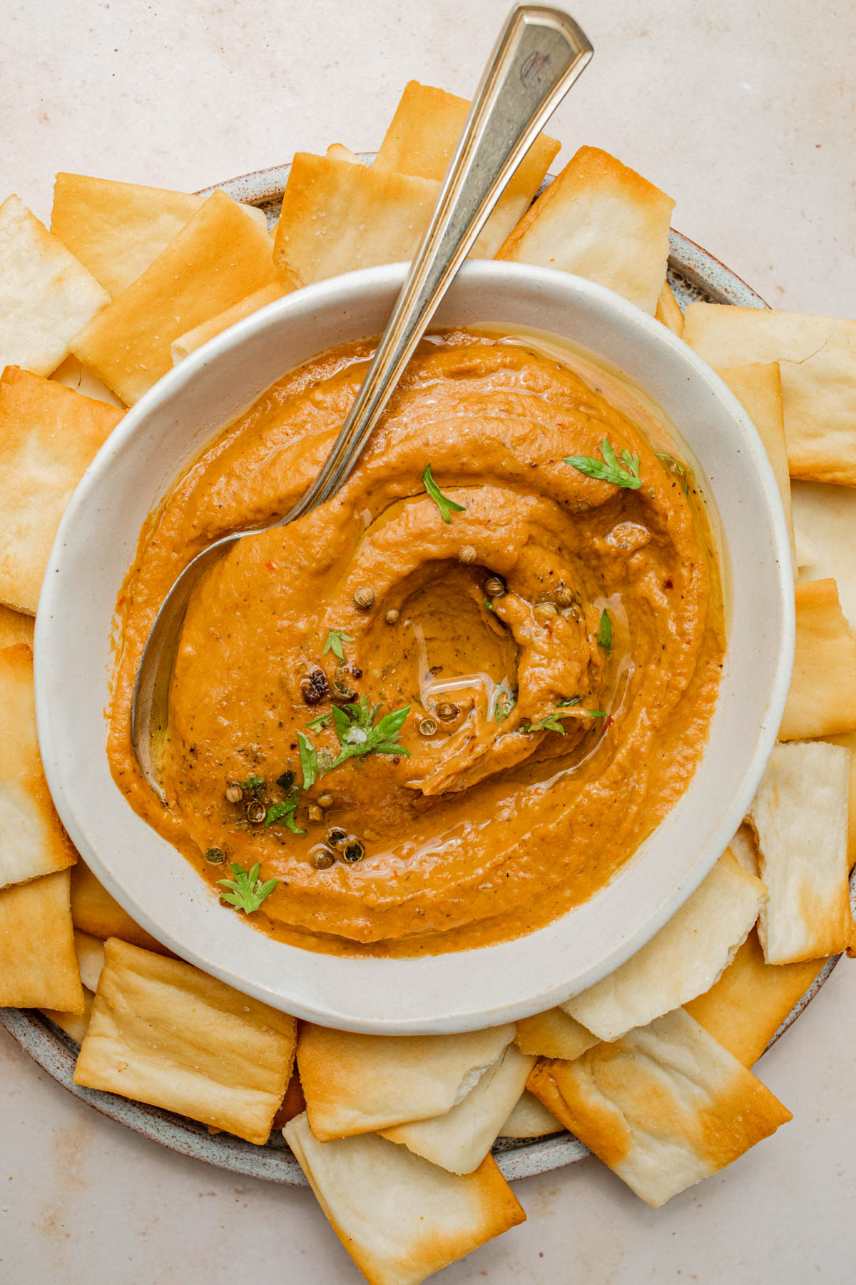 A bowl of red pepper dip surrounded with crackers.